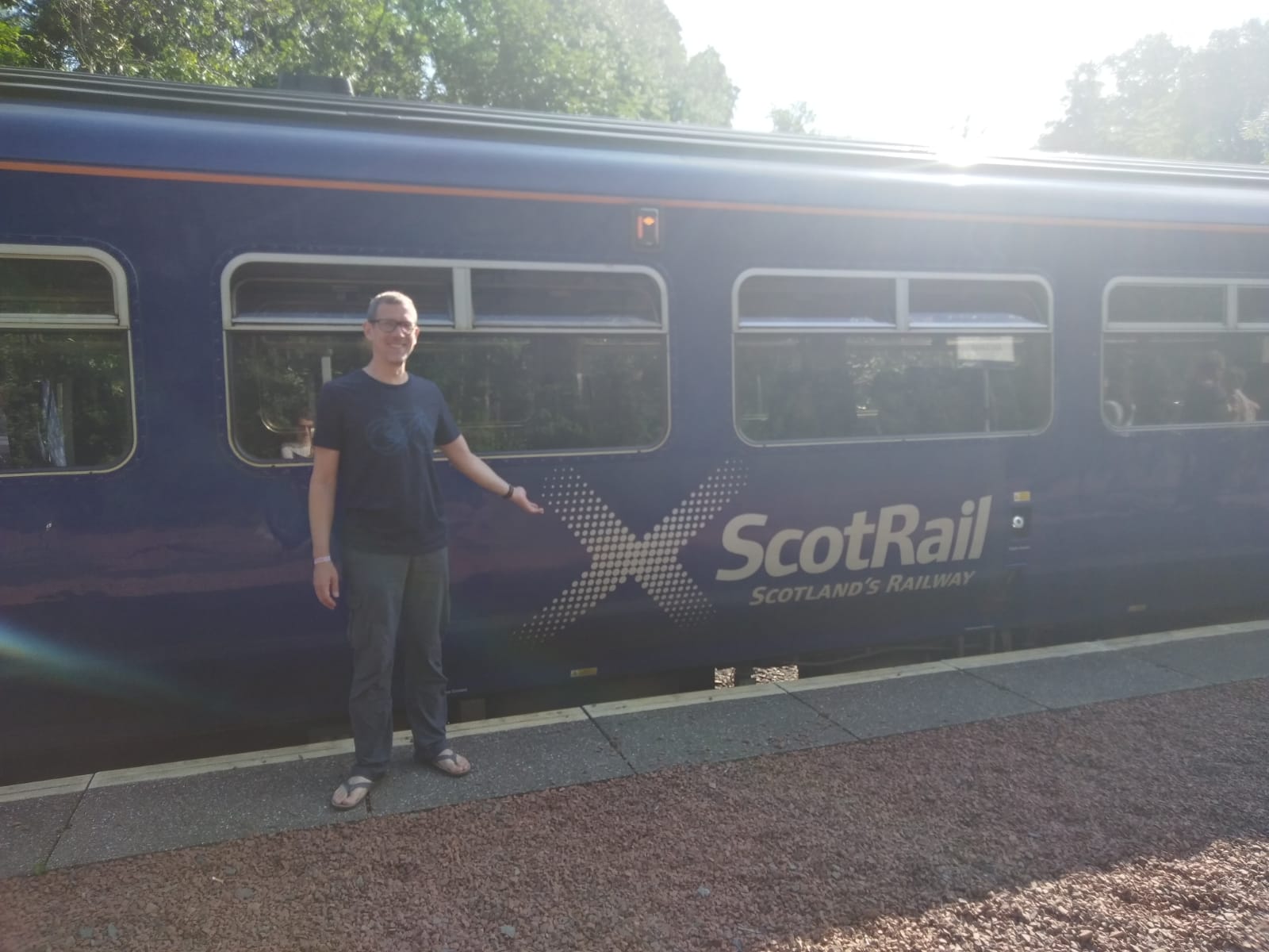 Me standing on a sunny platform in front of our train in the Scottish Highlands