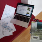 Laptop, sheets of paper and books on a red bench, all with information about Scotland