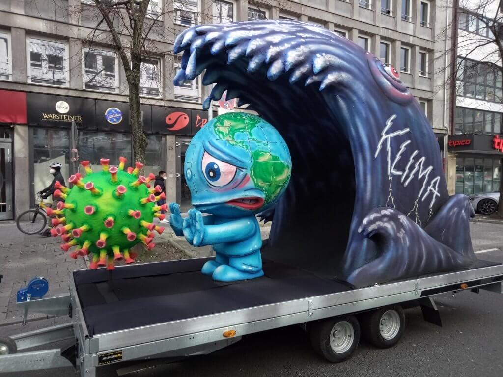 Float depicting earth as a creature trying to fend off the coronavirus before being hit by a tsunami wave of climate crisis