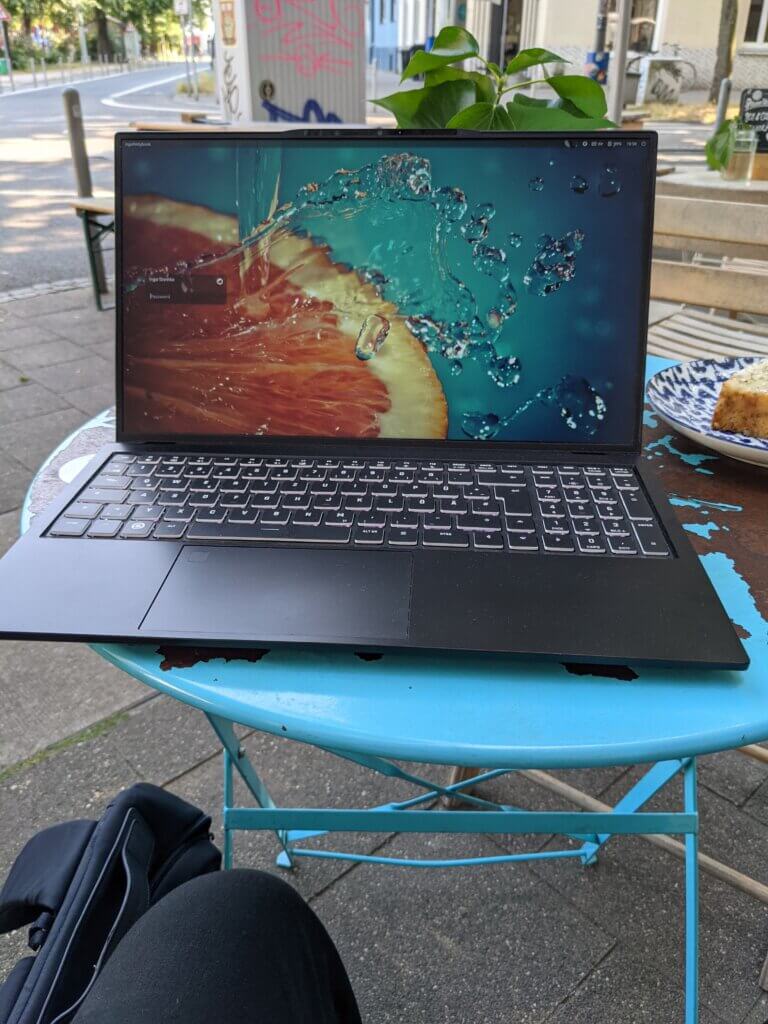 aufgeklappter Laptop-Computer mit Hintergrundbild einer Blutorange auf einem blauen Caféhaustisch