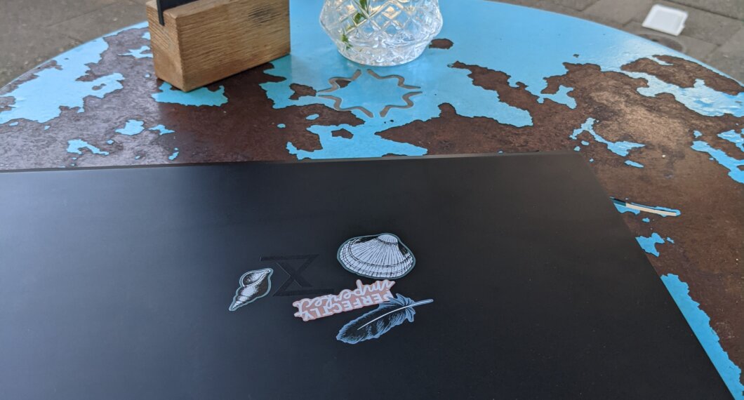 Schwarzes Laptop mit minimalistischen Aufklebern auf einem verranzten blauen Caféhaustisch in Düsseldorf