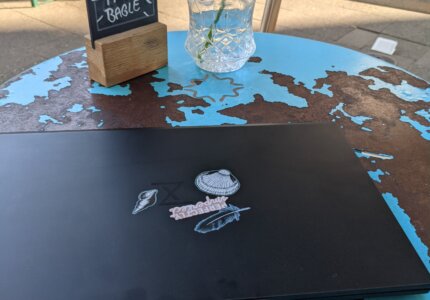 Schwarzes Laptop mit minimalistischen Aufklebern auf einem verranzten blauen Caféhaustisch in Düsseldorf