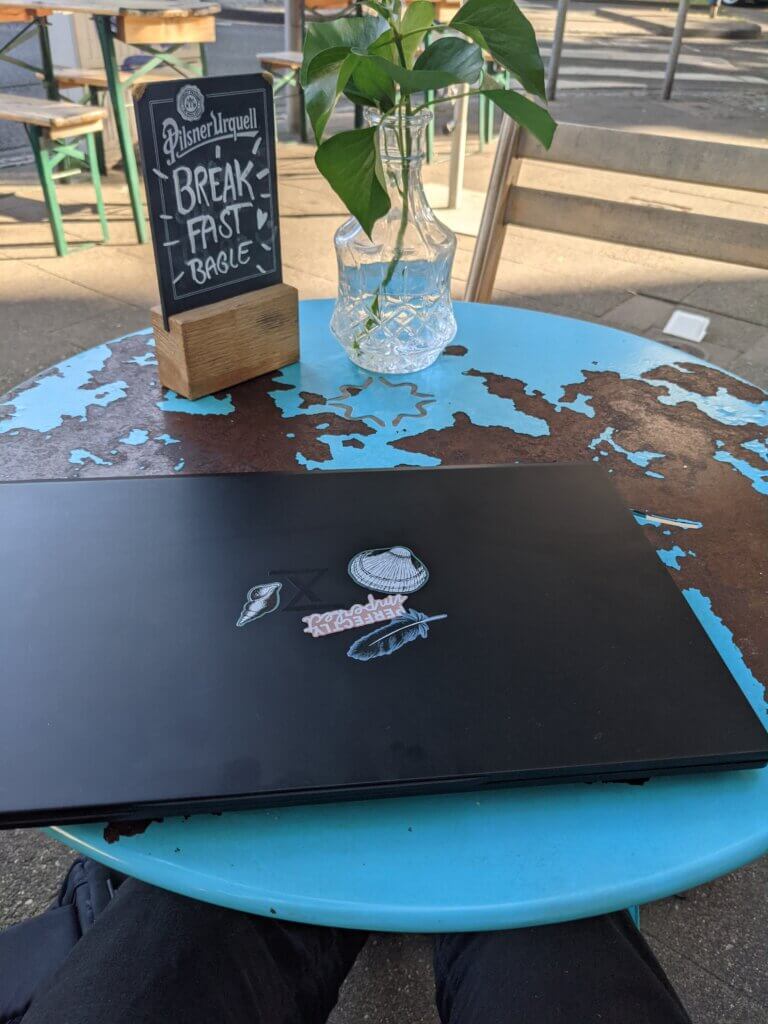 Schwarzes Laptop mit minimalistischen Aufklebern auf einem verranzten blauen Caféhaustisch