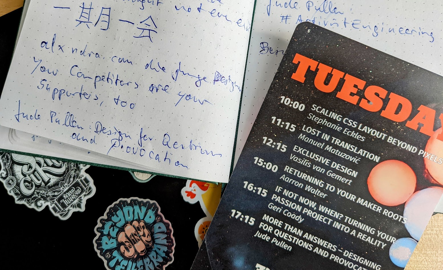 Sketchbook with notes in German and Japanese, laptop stickers by beyond tellerrand and stay curious, and the Tuesday schedule