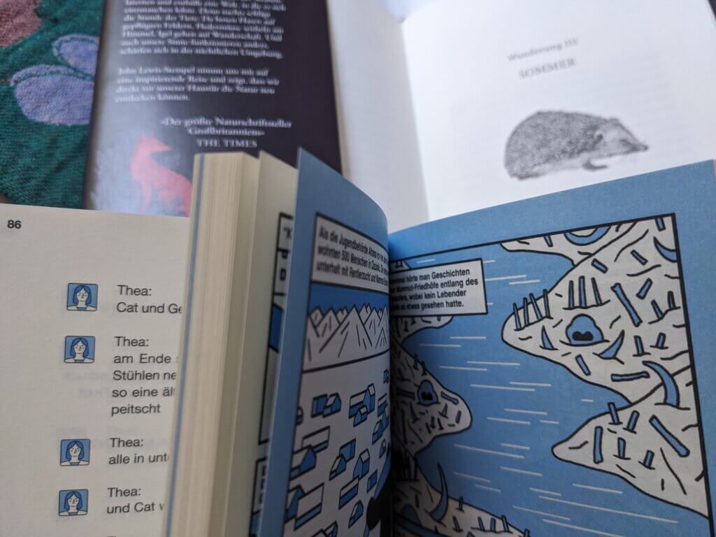 Bücher mit Einblick in die Graphic Novel und Chatromanelemente, im Hintegrund unscharf Illustrationen von Fuchs und Igel und ein Ausschnitt einer floralen Tischdecke