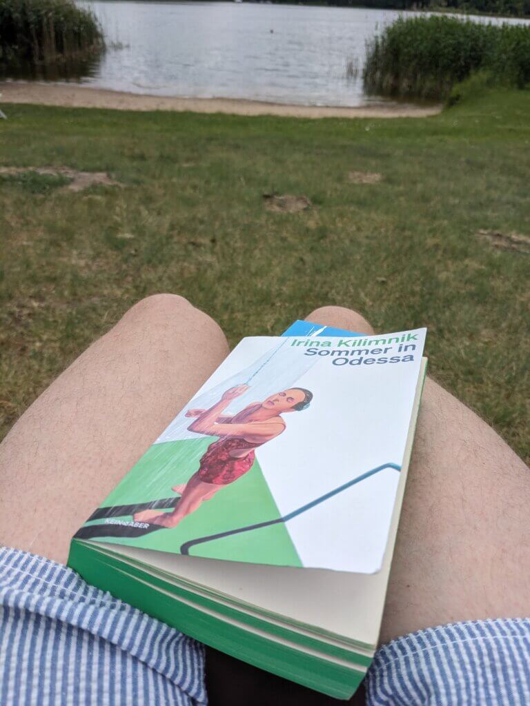 Buch Sommer in Odessa mit farbigen grünem Seitenschnitt auf einem Schoß mit Badeshorts über einer grünen Wiese