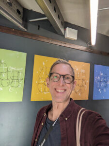 Ingo Steinke, smiling in front of colorful artwork